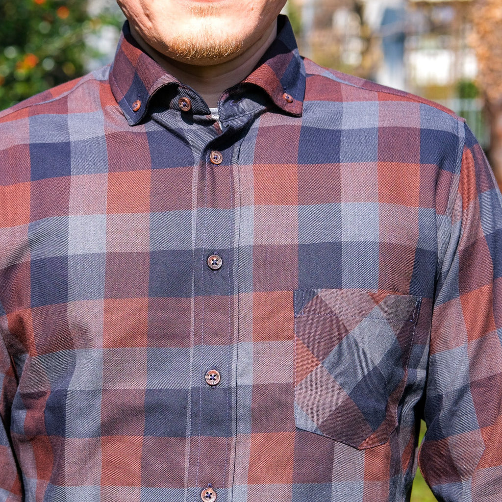 Person wearing a plaid shirt outdoors with greenery in the background