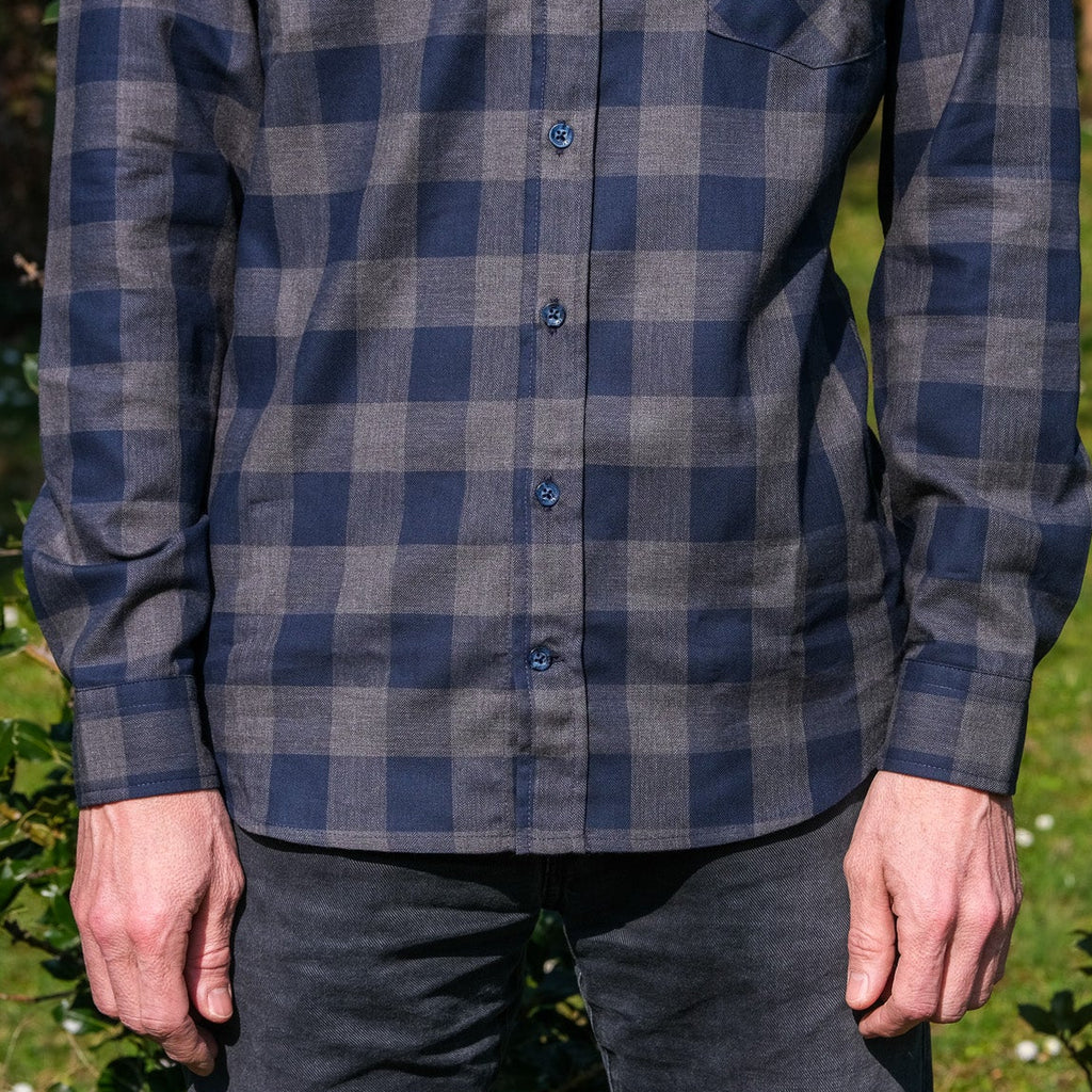 Person wearing a blue and gray plaid shirt outdoors on a grassy area.