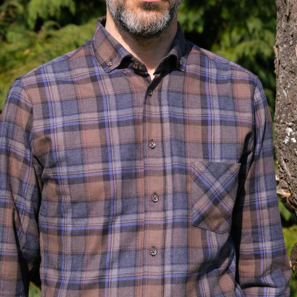 Man wearing a plaid shirt outdoors with greenery in the background